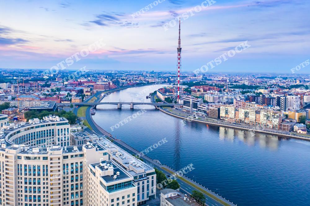 На фотографии изображена река Нева с видом на мосты и телебашню Санкт-Петербурга. Современные здания и исторические районы города гармонично сочетаются в одном кадре. Мягкий закатный свет подчеркивает линии архитектуры и спокойствие водной глади. Снимок передает атмосферу города, который соединяет прошлое и будущее.